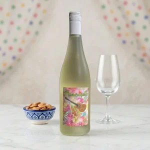 Botella de Vino Flamenquito Moscato Frizzante 5.5 en una mesa de mármol con almendras y una copa vacía, sugiriendo un aperitivo festivo.