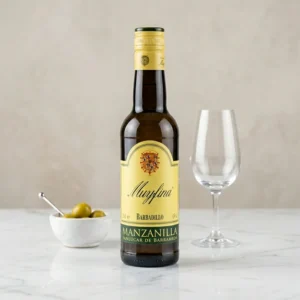 Botella de Vino Barbadillo Muy Fina Manzanilla Sanlúcar de Barrameda, servida con aceitunas y copa en ambiente de aperitivo.